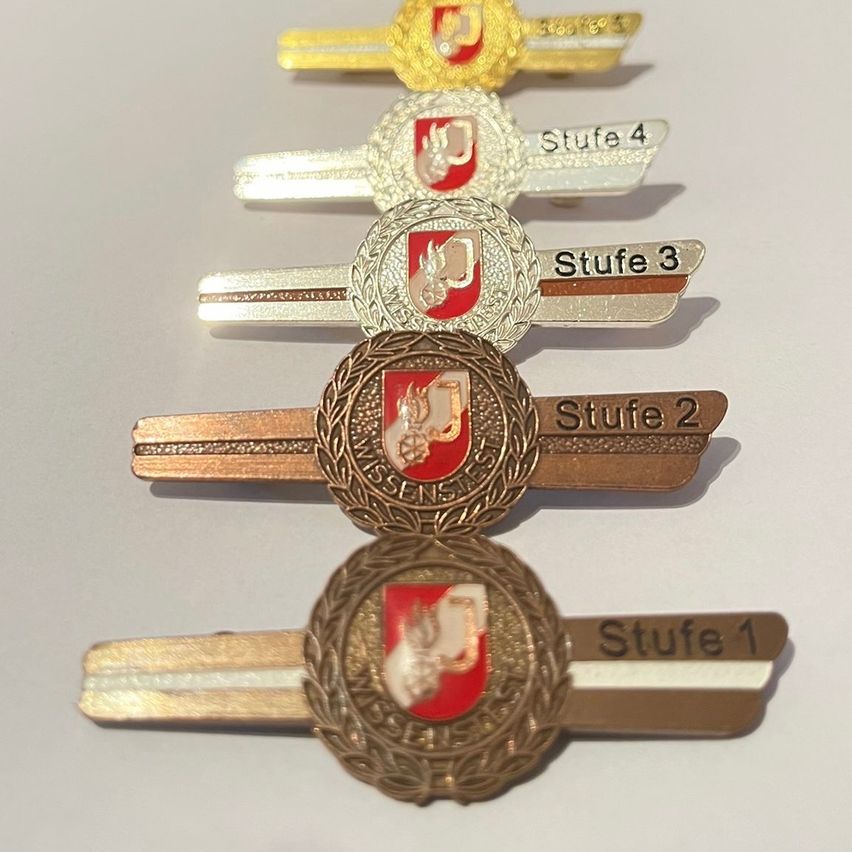 Fünf vertikal gestapelte Metallnadeln, jede mit einem roten Schild und einem weißen Design. Die Nadeln sind mit Stufe 1 bis Stufe 4 beschriftet.