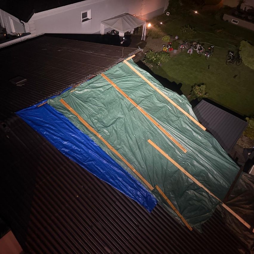 Eine Draufsicht auf ein Haus mit einem beschädigten Dach, das mit einem grünen Planen abgedeckt ist, der mit Holzstäben befestigt ist.