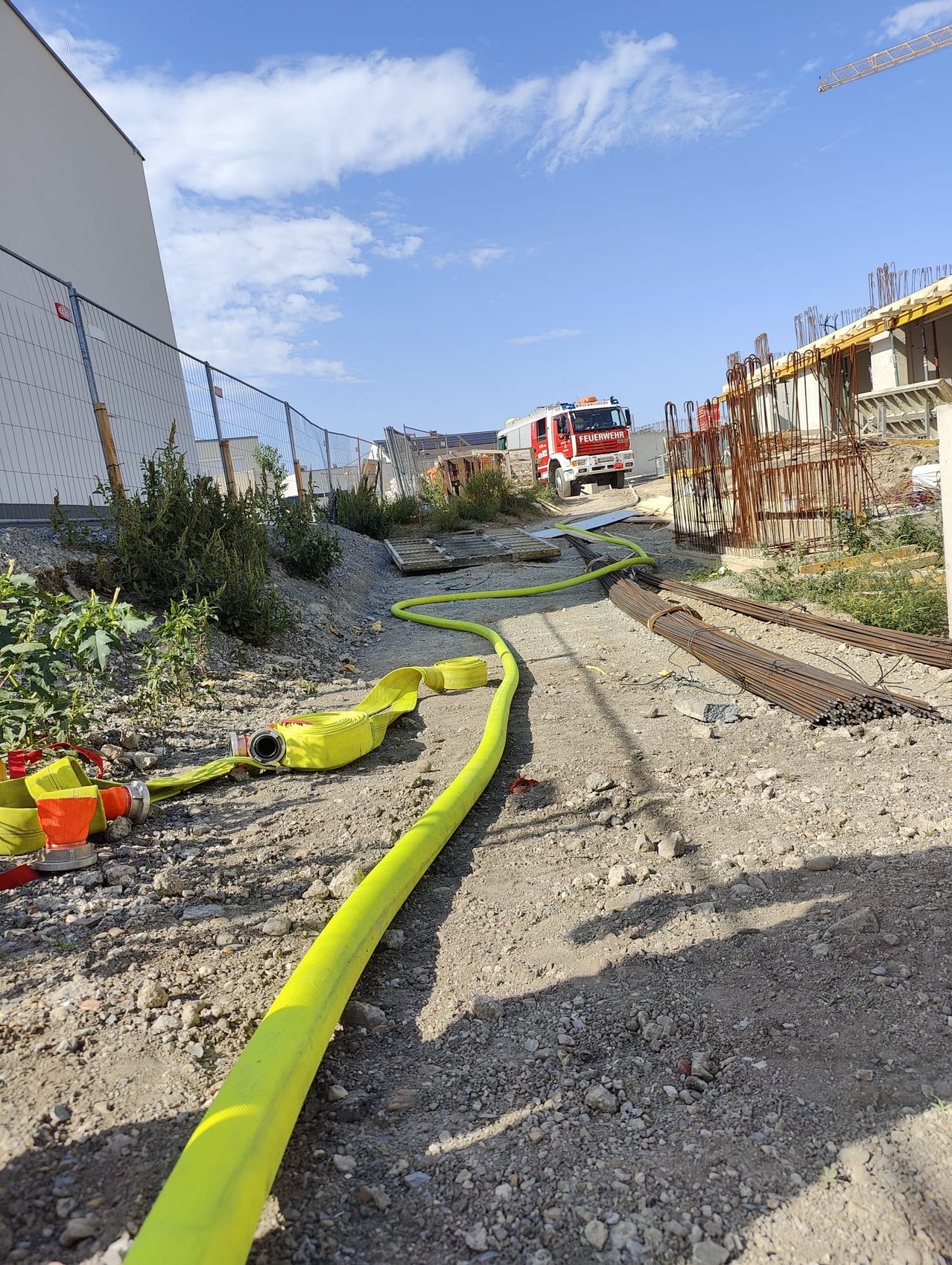 Ein Feuerwehrauto steht in der Nähe einer Baustelle mit gelben Schläuchen auf dem Boden.