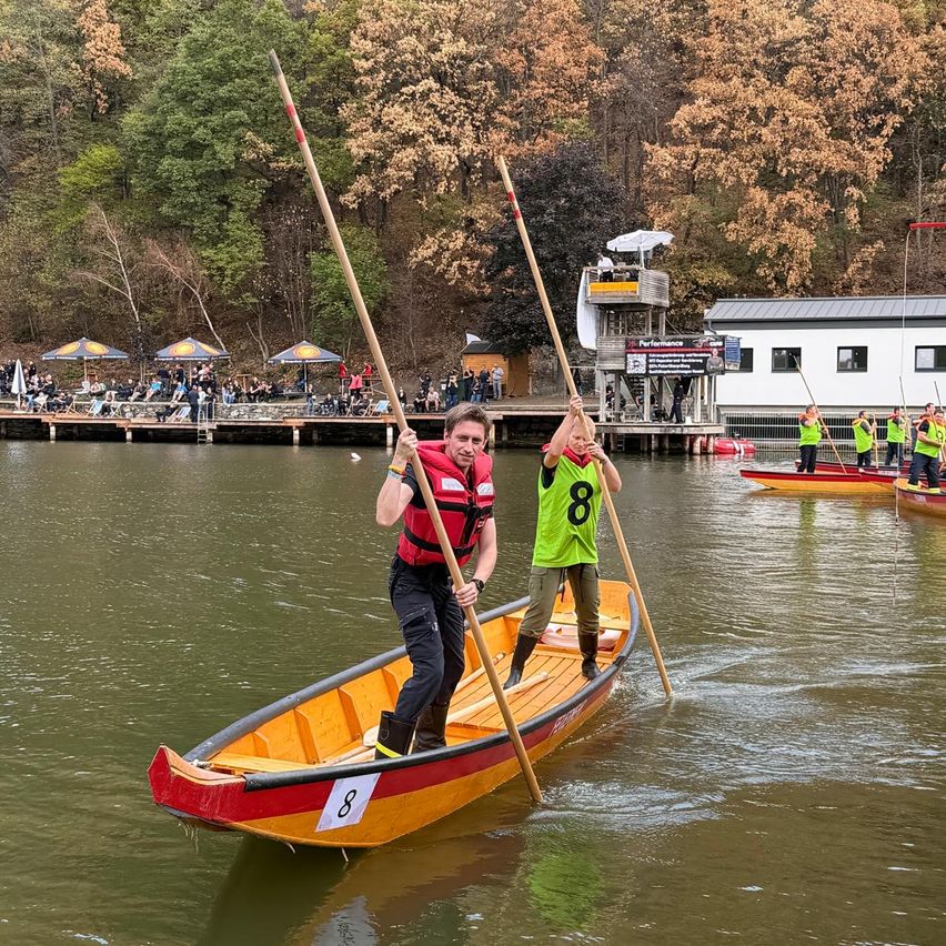 Ein Mann und ein Kind paddeln auf einem Fluss, mit Zuschauern am Ufer.