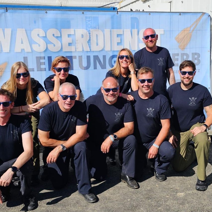 Eine Gruppe von Menschen in gleichen Uniformen posiert für ein Foto vor einem blauen Banner mit weißem Text.
