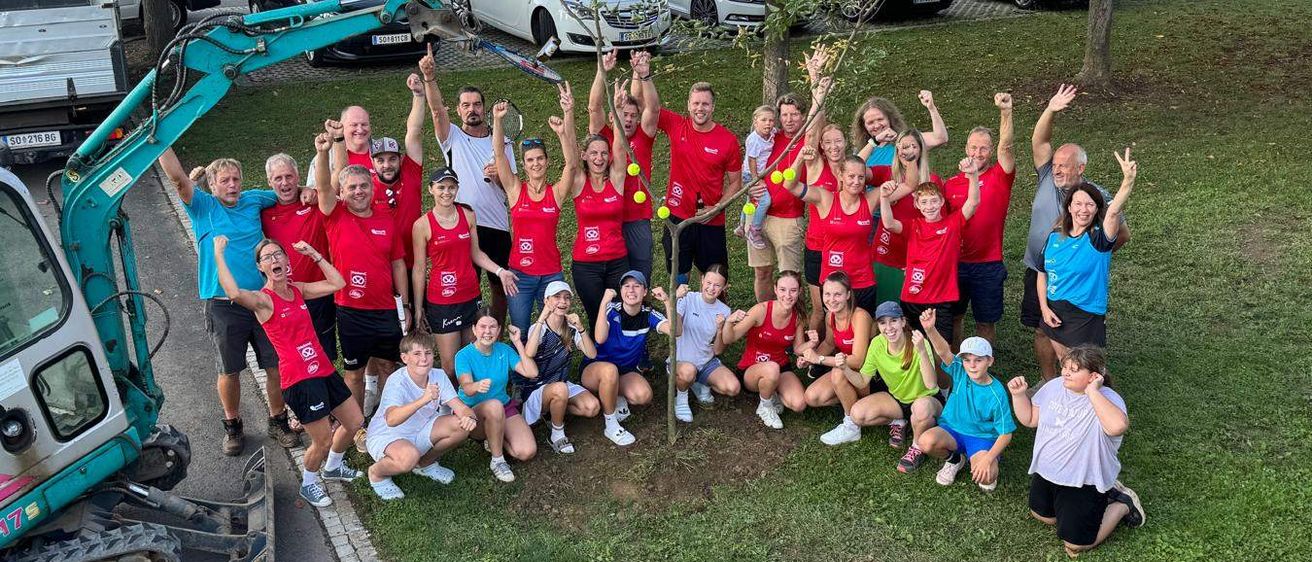 Eine Gruppe von Menschen in Rot und Blau posiert für ein Foto im Park. Sie halten Tennisschläger und haben Tennisbälle um den Hals.