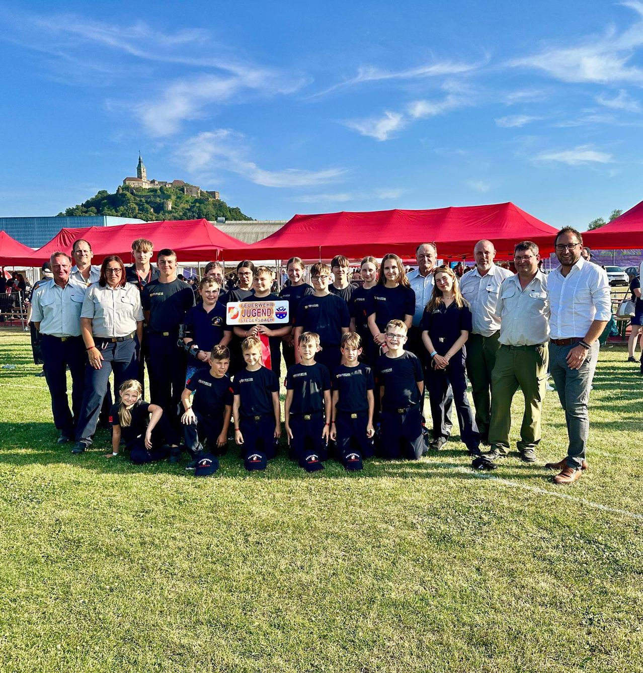 Eine Gruppe von Erwachsenen und Kindern posiert für ein Foto auf einem Rasenfeld, mit roten Zelten im Hintergrund.