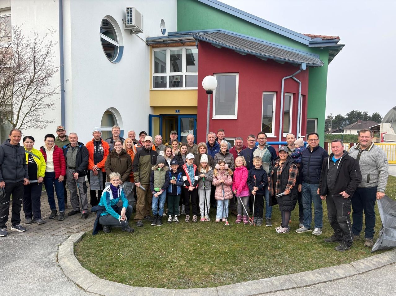 Eine Gruppe von Menschen in Winterkleidung steht vor einem Gebäude mit roten, gelben und grünen Wänden. Einige halten Stöcke, und andere tragen Mützen.