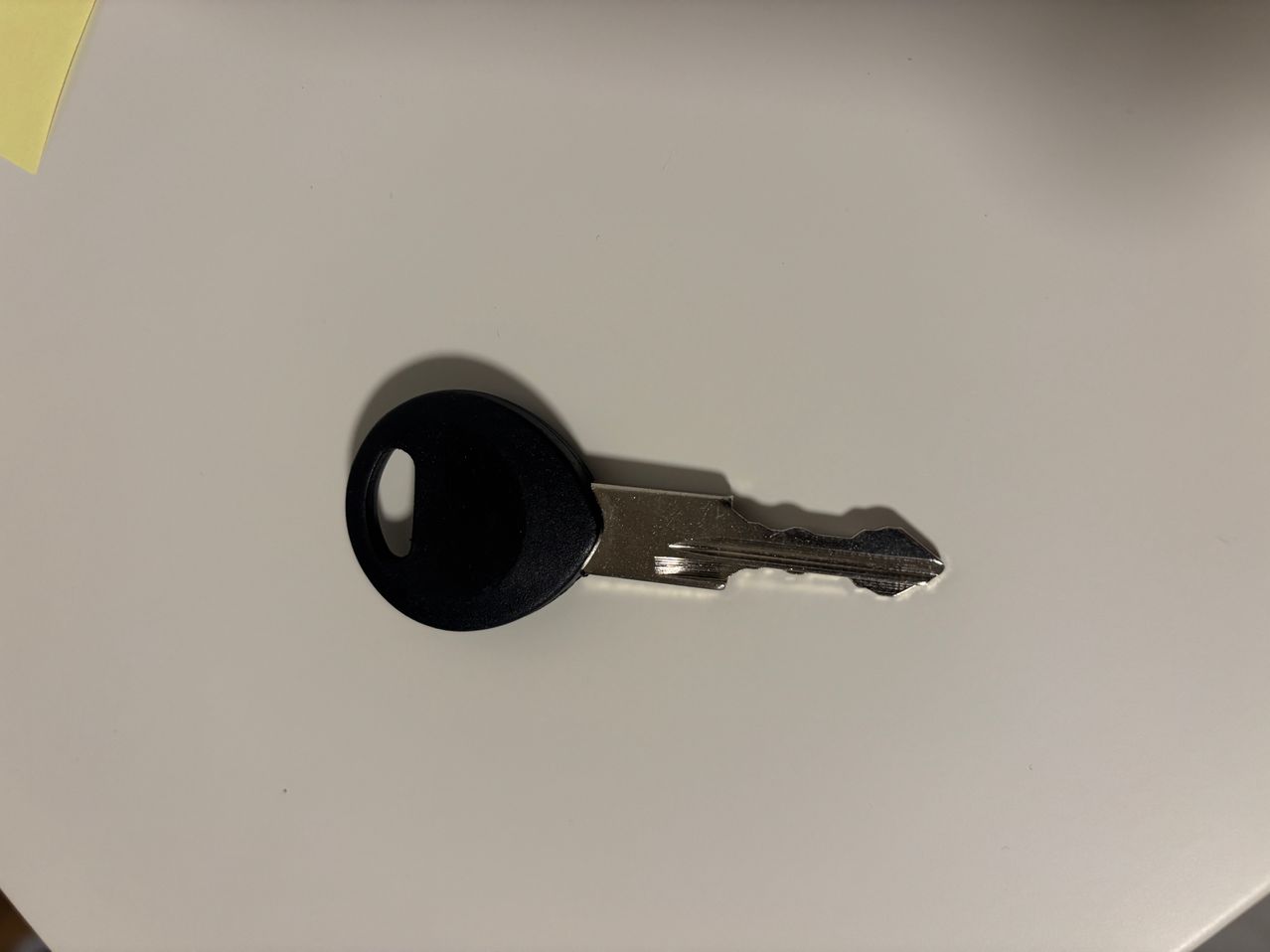 Ein schwarzer Kunststoffschlüssel mit silbernem Metall liegt flach auf einer weißen Oberfläche.