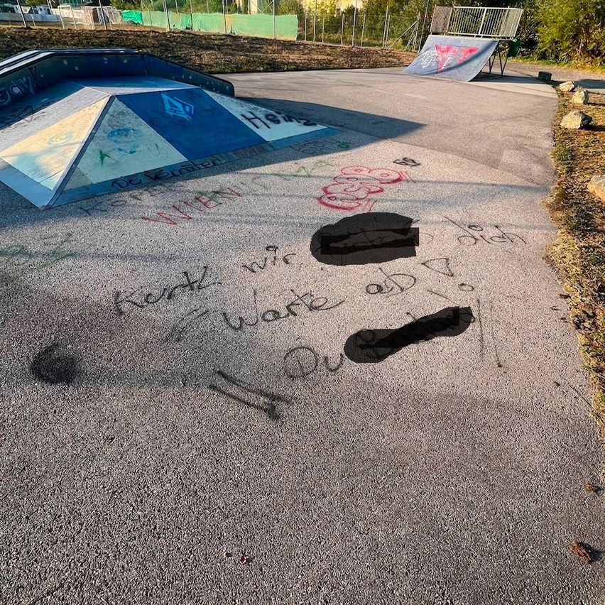 Ein Skatepark mit Graffiti auf dem Boden und einer Rampe im Hintergrund. Die Graffiti enthält die Wörter 'Kerk' und 'work above'.