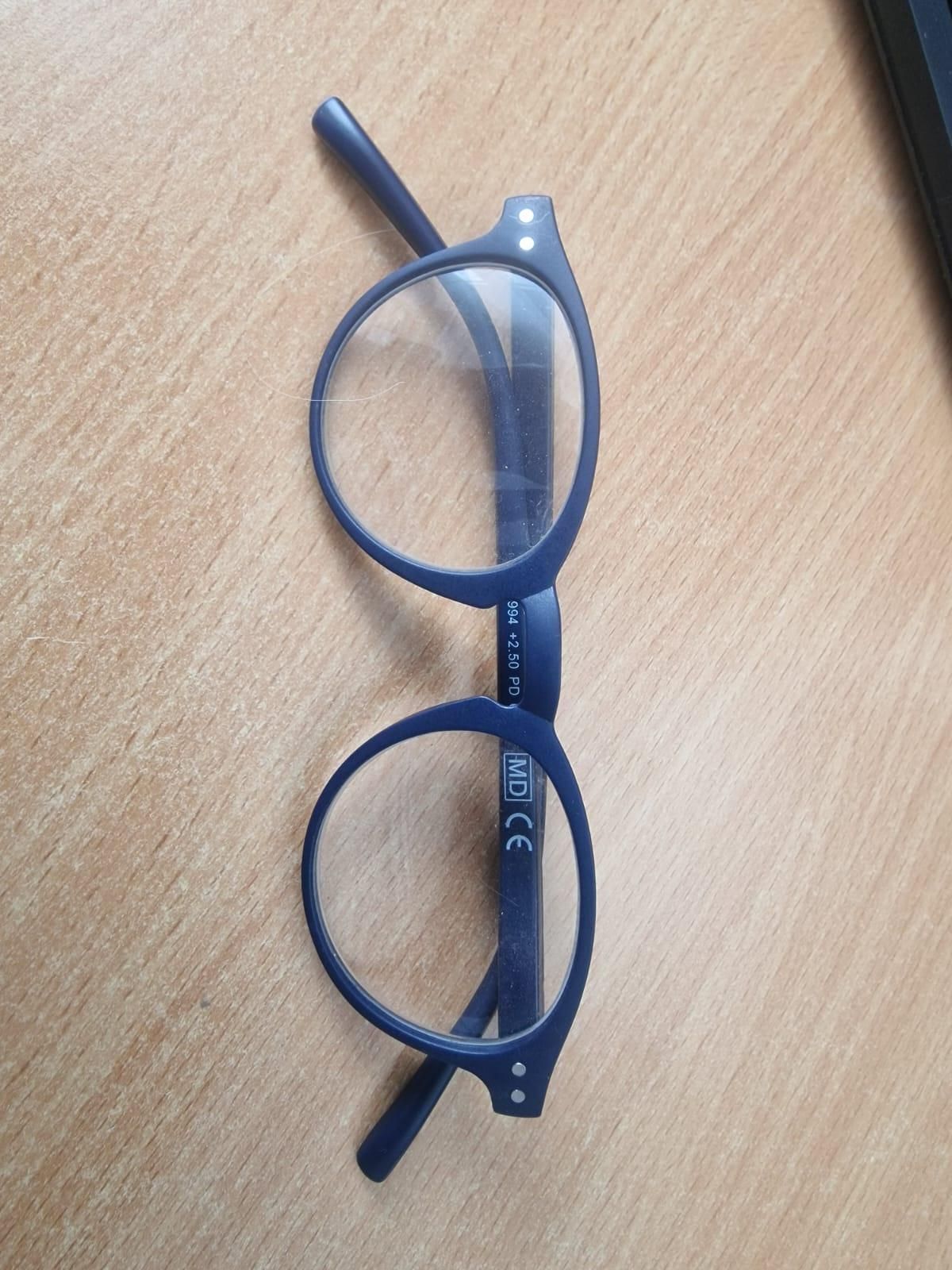 Ein Paar blauer Brille mit klaren Gläsern und einer Markenbezeichnung auf dem rechten Glas. Die Gläser haben eine leichte Krümmung.