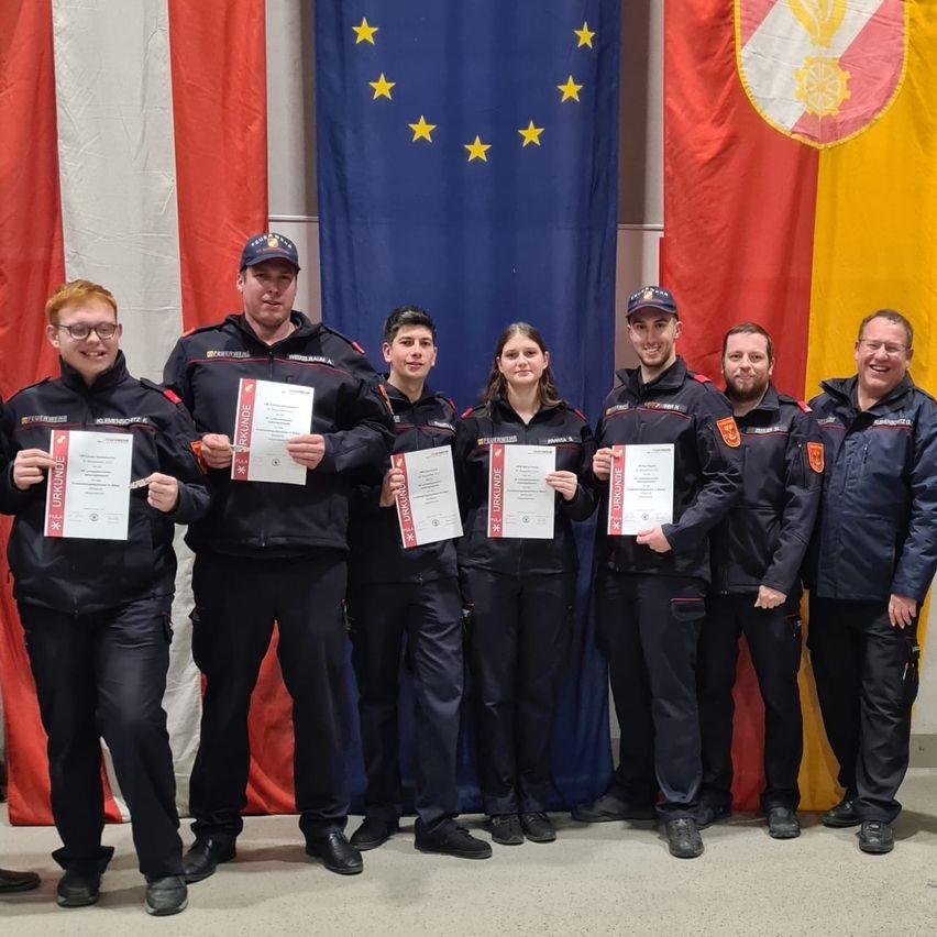 Eine Gruppe uniformierter Personen, die Urkunden halten, posiert für ein Foto vor Flaggen, einschließlich der Flagge der Europäischen Union und der deutschen Flagge.