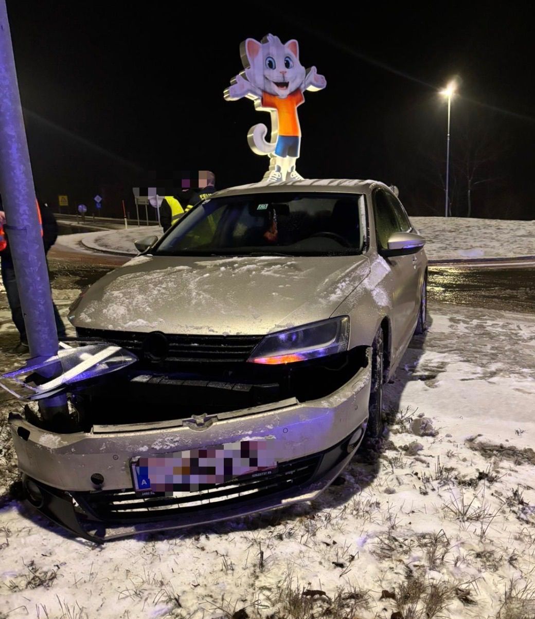 Ein Auto mit beschädigter Front steht auf schneebedecktem Boden bei Nacht. Ein Maskottchen steht auf dem Dach.
