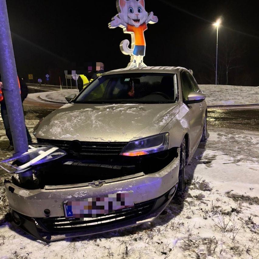 Ein Auto mit beschädigter Front steht auf schneebedecktem Boden bei Nacht. Ein Maskottchen steht auf dem Dach.