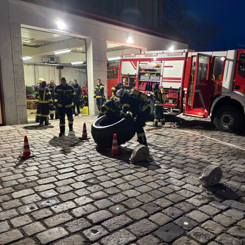 Feuerwehrleute üben eine Reifenrettung vor der Feuerwache. Ein Feuerwehrmann ist dabei zu sehen, wie er an einem großen Reifen arbeitet.