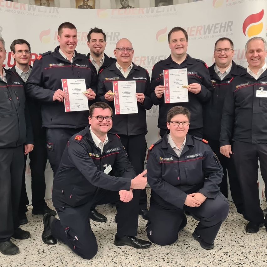 Eine Gruppe von Menschen in Uniformen posiert für ein Foto mit Zertifikaten. Der Mann, der kniet, gibt einen Daumen hoch.