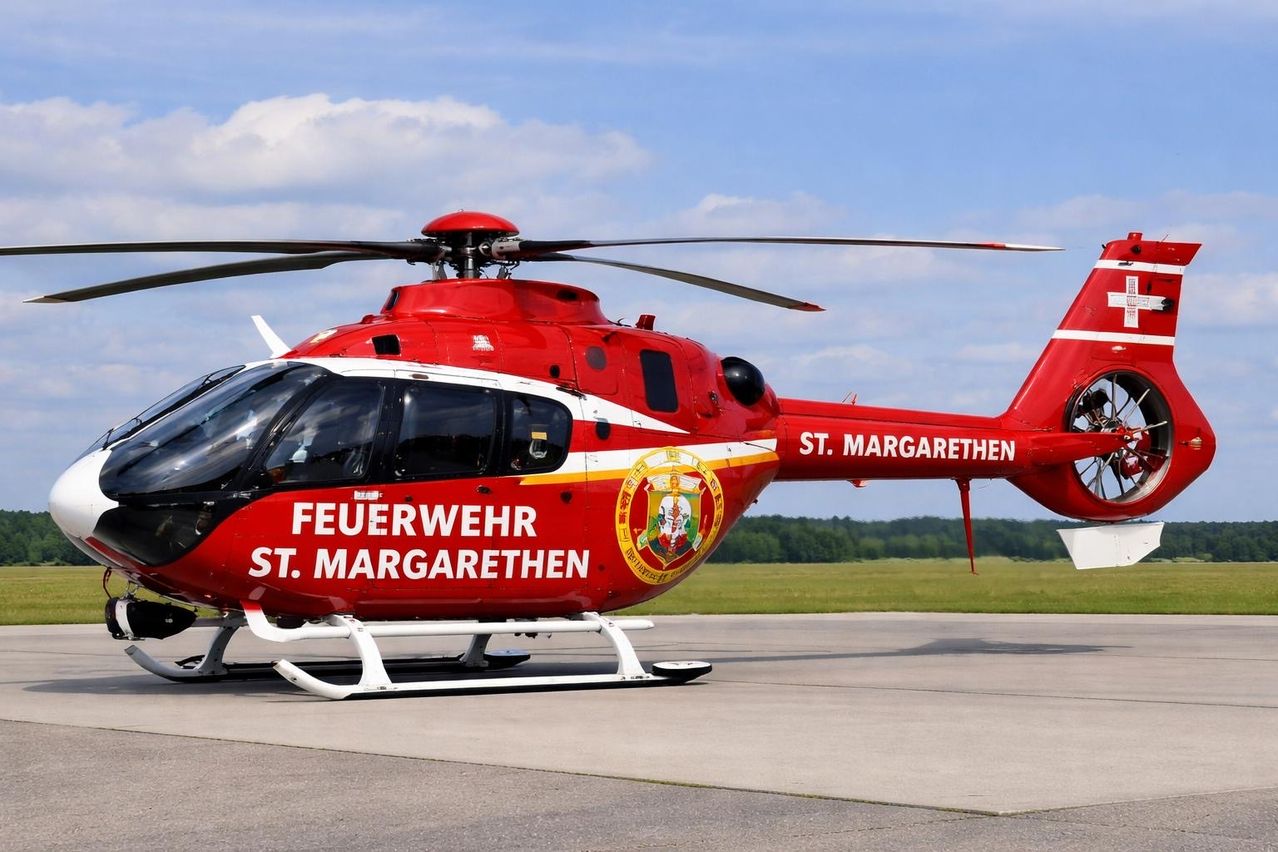 Ein roter Hubschrauber mit 'FEUERWEHR ST. MARGARETHEN' auf der Seite und einem Logo steht auf der Landebahn.