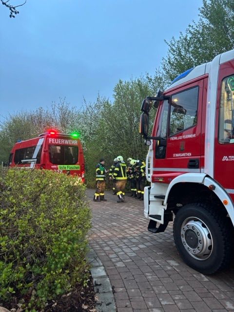 Eine Gruppe Feuerwehrleute in gelben Uniformen steht neben einem roten Feuerwehrauto mit einer roten Lampe oben, möglicherweise in Vorbereitung auf einen Notfall.