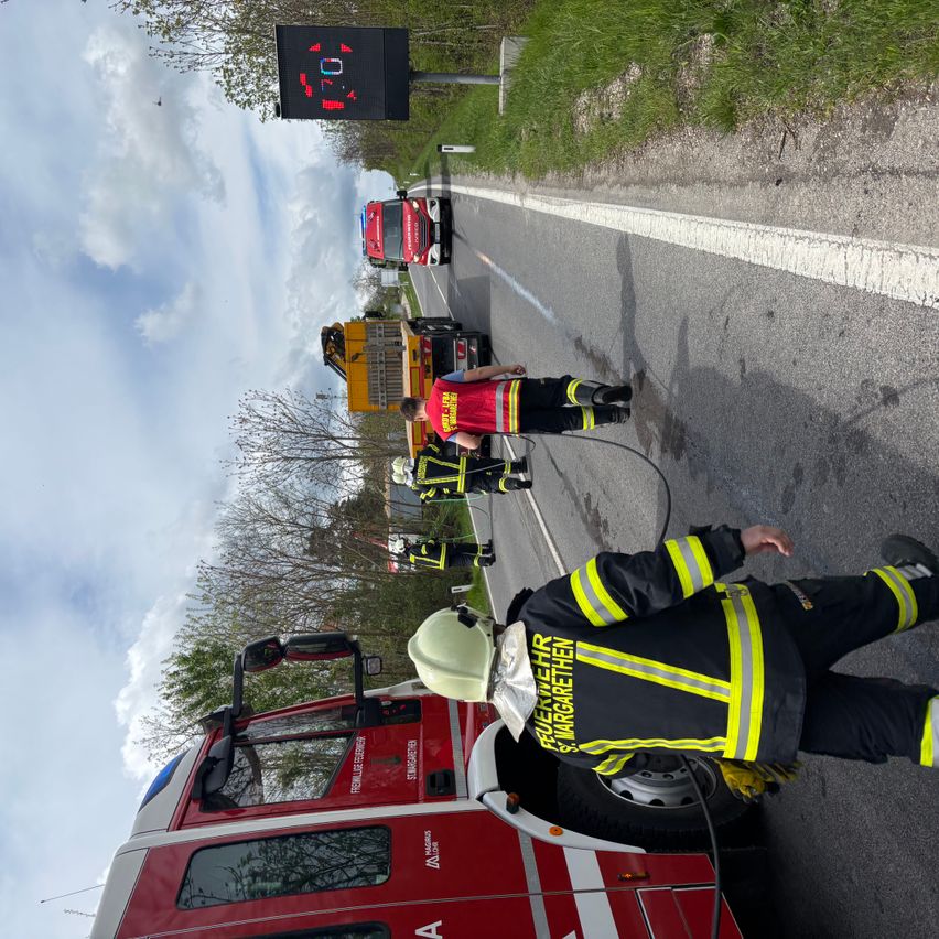 Rettungskräfte in gelben und schwarzen Uniformen kümmern sich um ein Fahrzeug auf einer Straße. Ein elektronisches Geschwindigkeitslimitschild ist oben sichtbar.