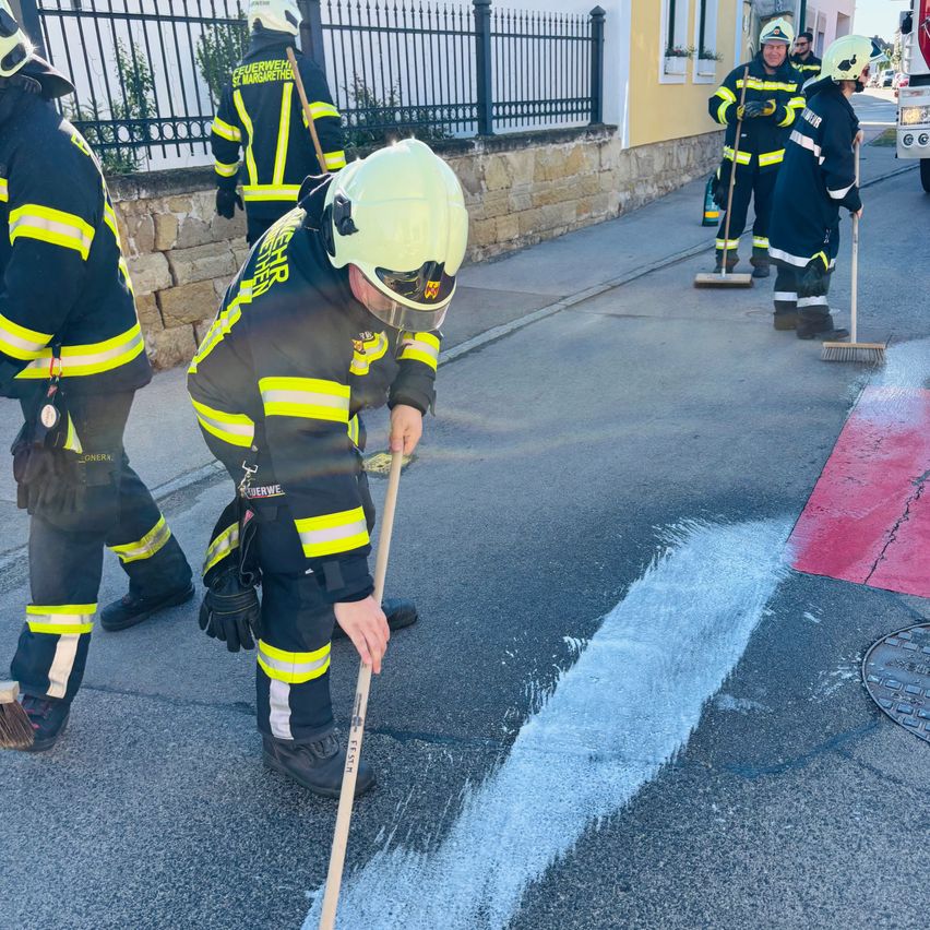 Feuerwehrleute in Uniform malen die Straße mit weißen und roten Markierungen. Eine Person benutzt einen Besen, um weißen Farbe zu verteilen.