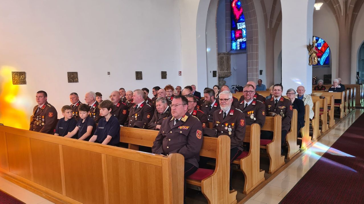 Eine Gruppe von Menschen, darunter uniformierte Personen, sitzt in einer Kirchenbank mit Blick nach vorne, im Hintergrund ein Buntglasfenster.