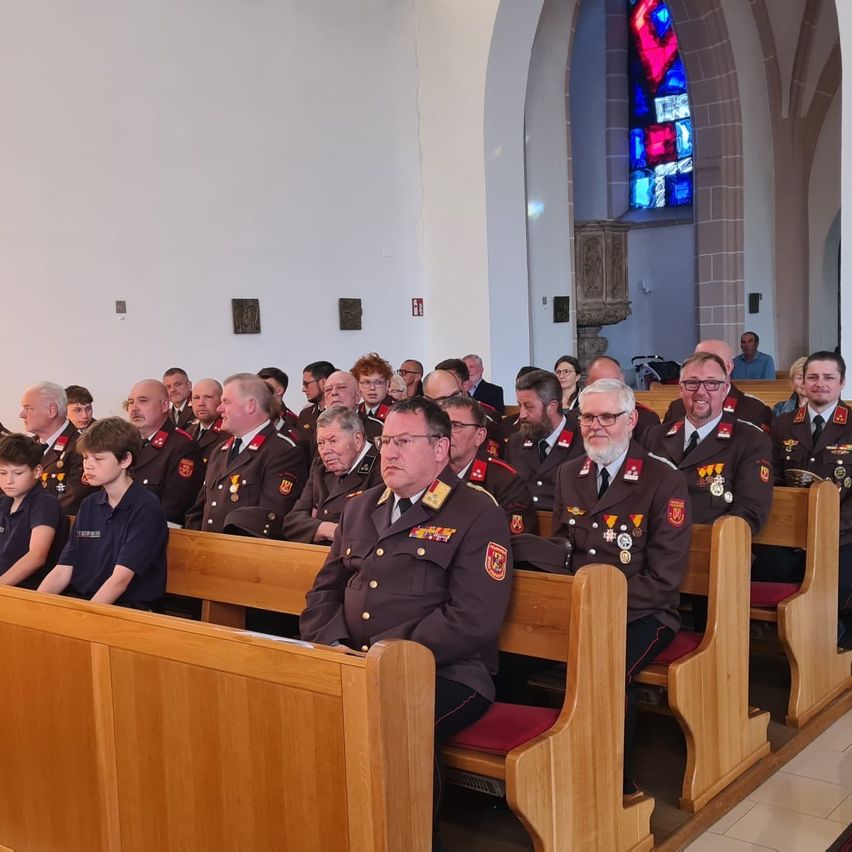 Eine Gruppe von Menschen, darunter uniformierte Personen, sitzt in einer Kirchenbank mit Blick nach vorne, im Hintergrund ein Buntglasfenster.
