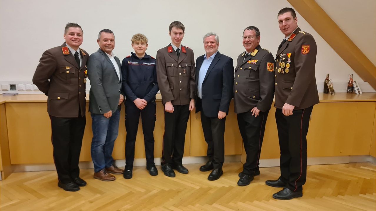 Eine Gruppe von Männern in Uniformen und Anzügen posiert für ein Foto in einer Innenumgebung.