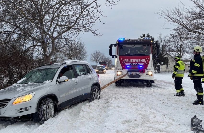 Ein schneebedeckter SUV steckt im Schnee fest und wird von einem Feuerwehrauto mit Feuerwehrleuten gezogen.