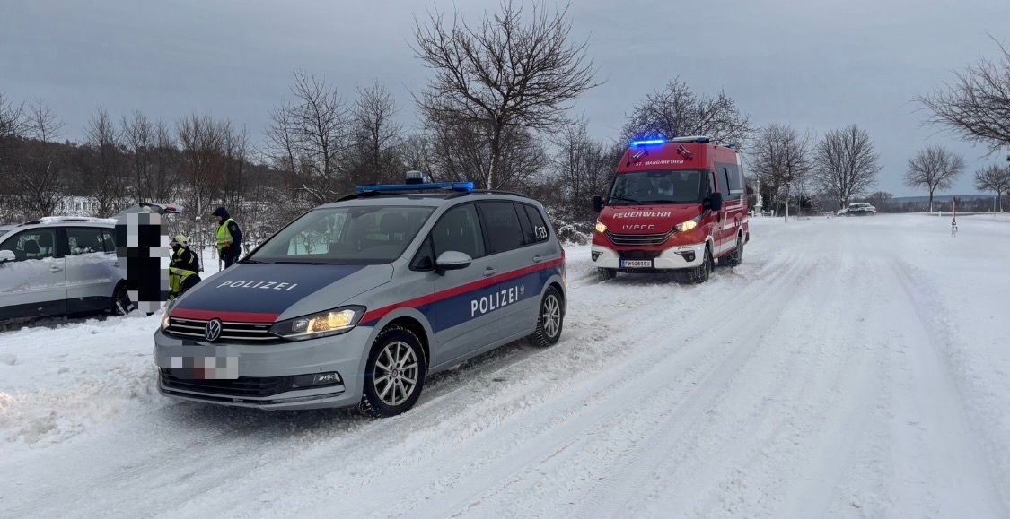 Ein Polizeiauto und ein Feuerwehrfahrzeug sind auf einer verschneiten Straße geparkt, mit zwei Personen in reflektierenden Westen in der Nähe.