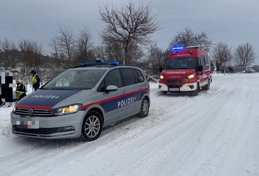 Ein Polizeiauto und ein Feuerwehrfahrzeug sind auf einer verschneiten Straße geparkt, mit zwei Personen in reflektierenden Westen in der Nähe.