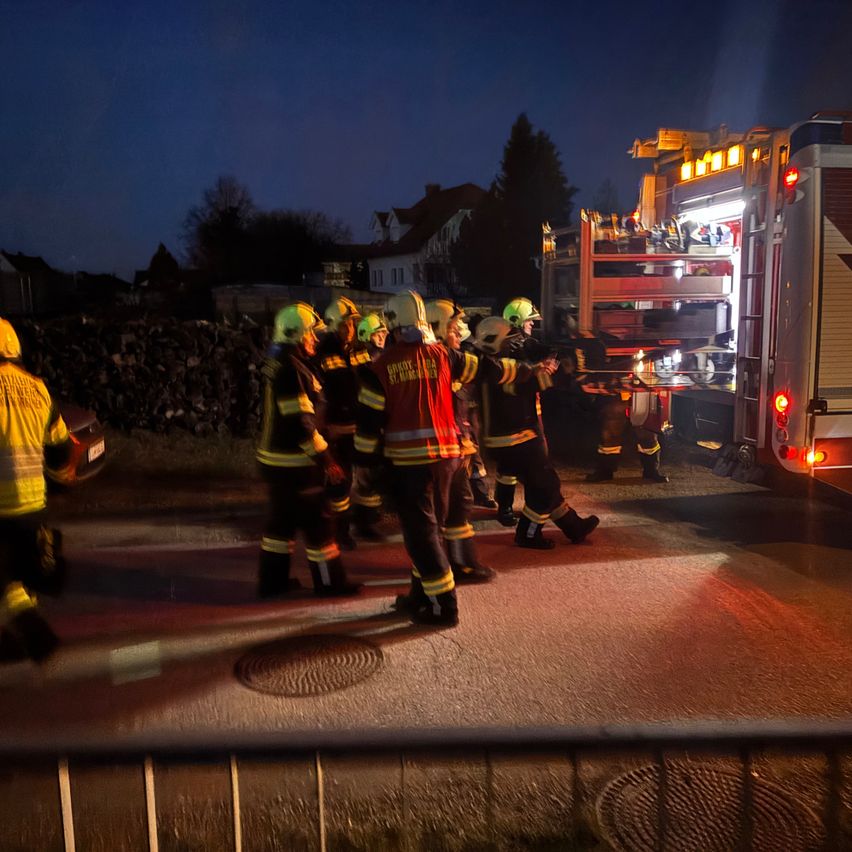 Feuerwehrleute in gelben und roten Uniformen versammeln sich nachts um einen Feuerwehrwagen. Die Lichter des Wagens sind eingeschaltet und beleuchten die Szene. Sie bereiten sich wahrscheinlich auf einen Notfall vor.