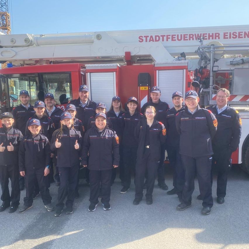 Eine Gruppe von Feuerwehrleuten und Freiwilligen steht vor einem Feuerwehrauto mit der Aufschrift 'Stadtfeuerwehr Eisen'.