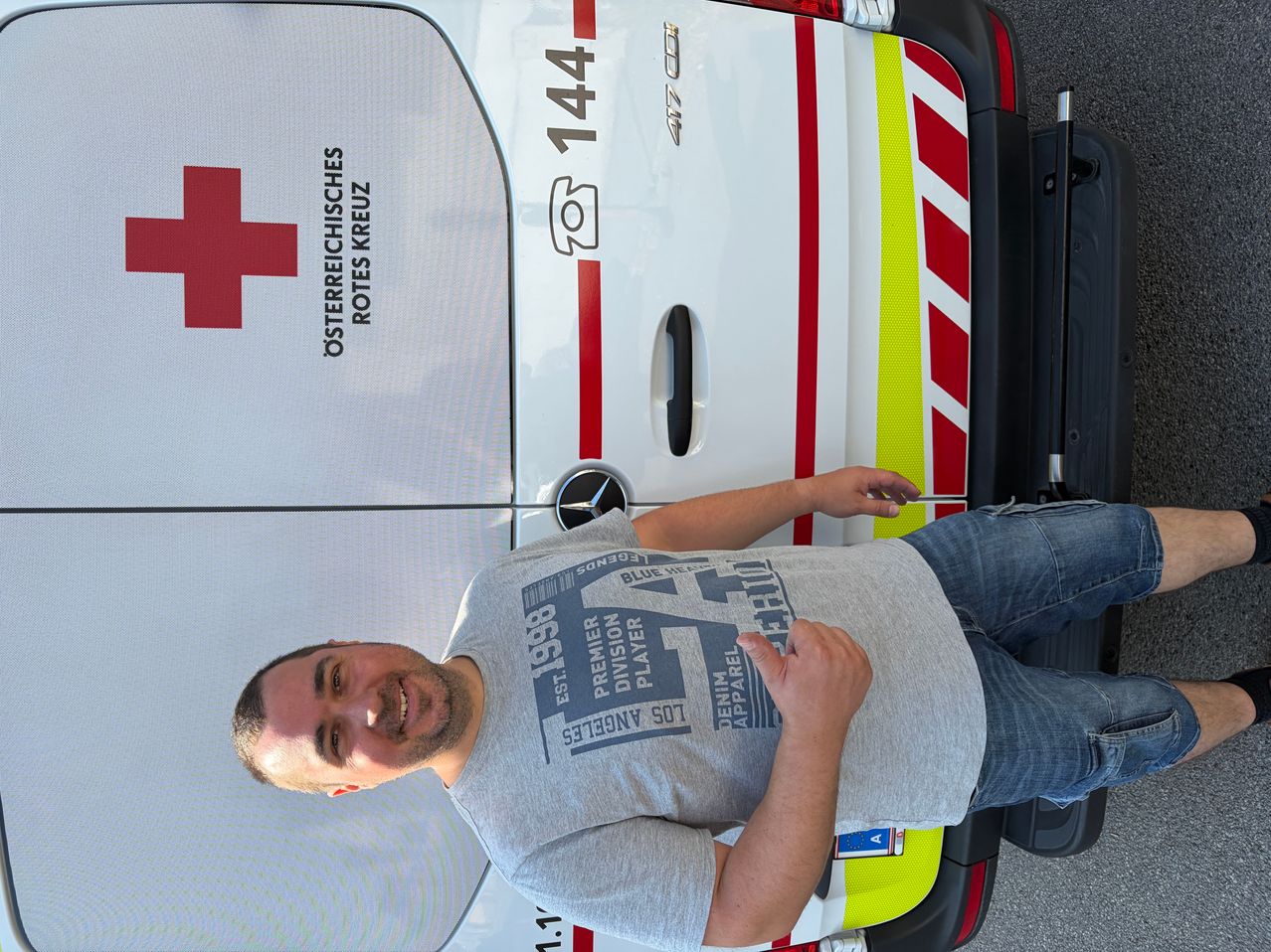 Ein Mann in einem grauen T-Shirt liegt auf der Rückseite eines Rettungswagens mit der Nummer 144 an der Seite.