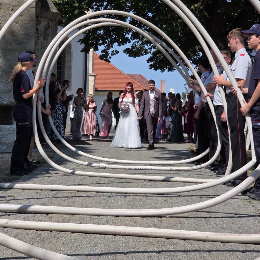 Eine Braut geht durch einen Tunnel aus Rohren, während Gäste auf beiden Seiten stehen, einige in Uniform.