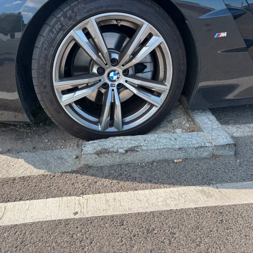 Nahaufnahme des vorderen Rades und Reifens eines schwarzen BMW-Autos am Straßenrand.