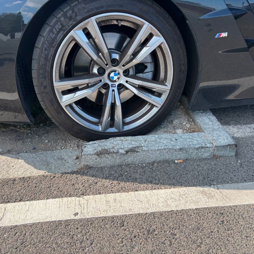 Nahaufnahme des vorderen Rades und Reifens eines schwarzen BMW-Autos am Straßenrand.