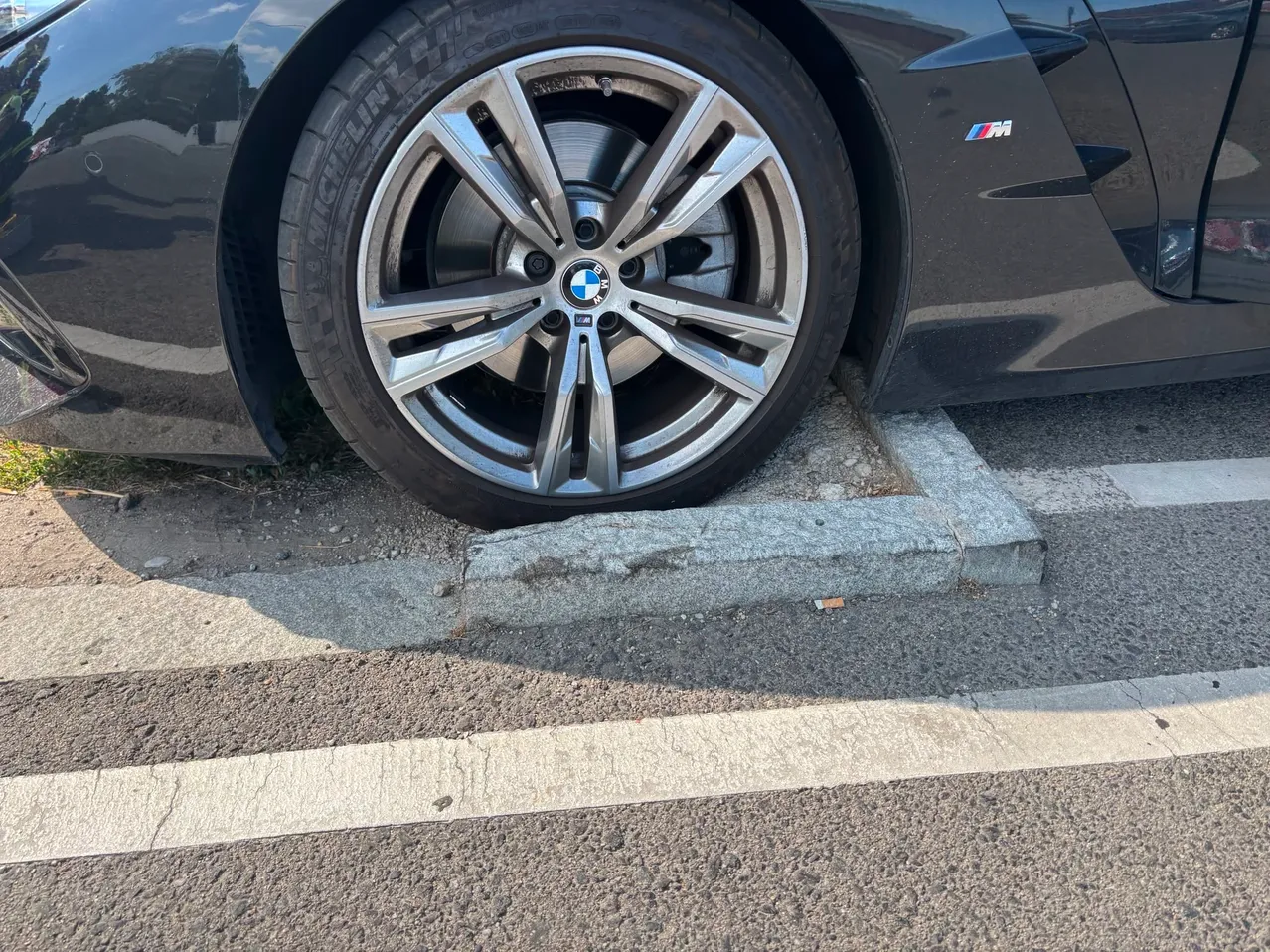 Nahaufnahme des vorderen Rades und Reifens eines schwarzen BMW-Autos am Straßenrand.