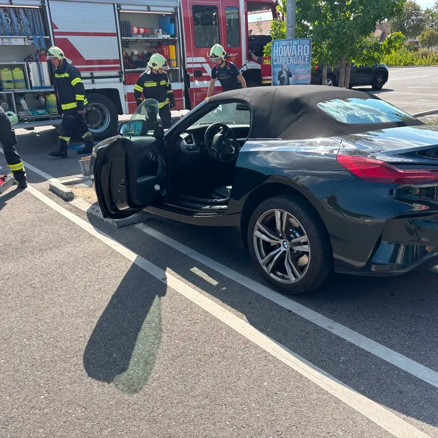 Ein schwarzer BMW Z4 Roadster mit geöffneten Türen, am Straßenrand geparkt, mit Feuerwehrleuten in der Nähe.