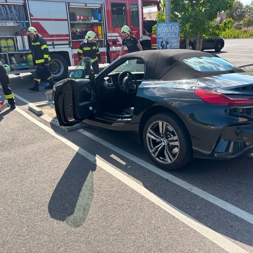 Ein schwarzer BMW Z4 Roadster mit geöffneten Türen, am Straßenrand geparkt, mit Feuerwehrleuten in der Nähe.