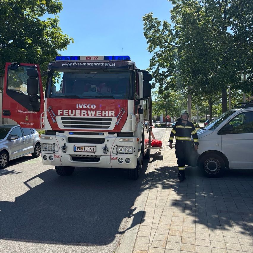 Ein roter Iveco-Feuerwehrwagen mit offenen Türen und ein Feuerwehrmann neben einem weißen Van auf einer Straße.