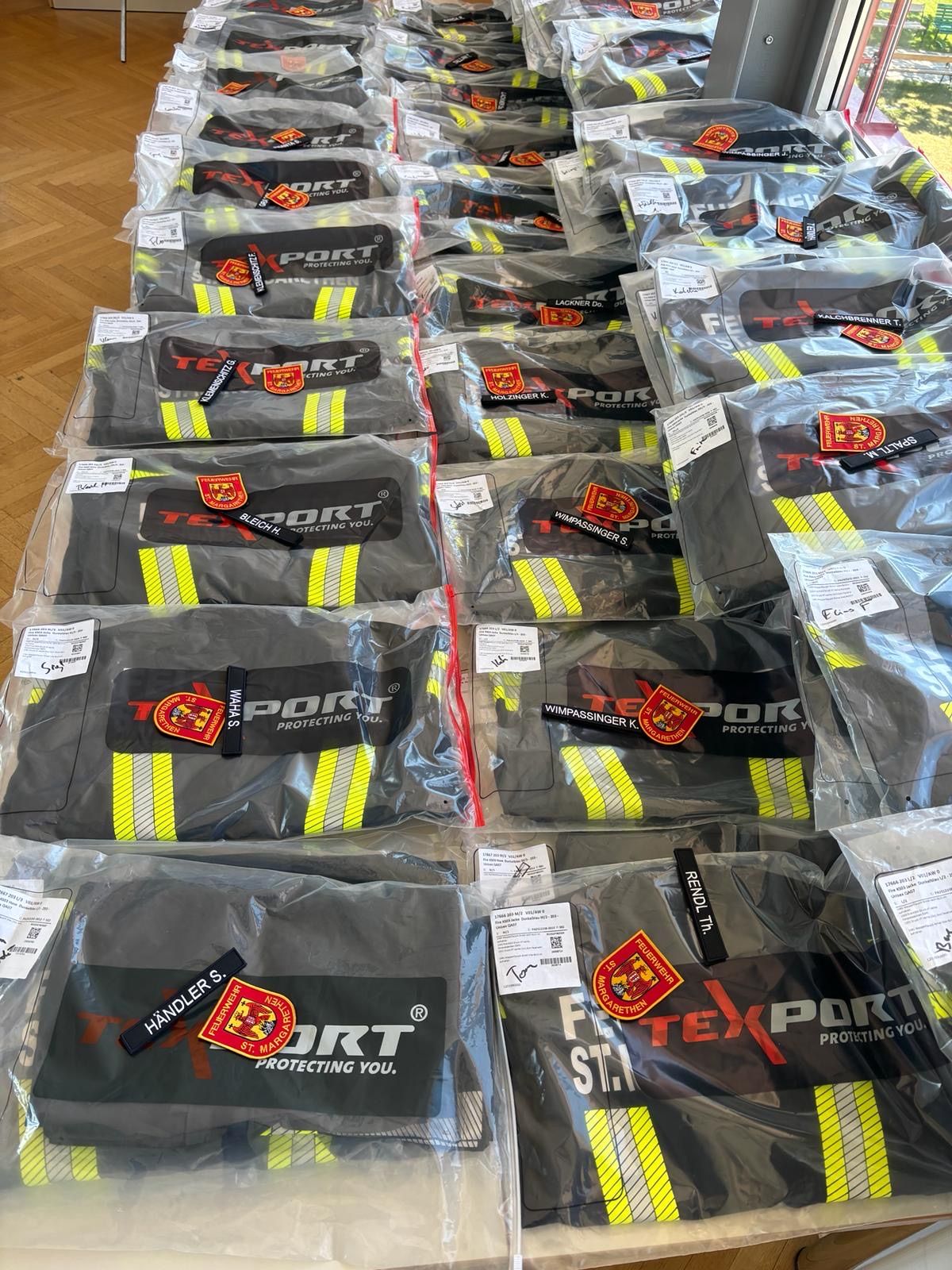 Mehrere Packungen von Schutzausrüstung, wahrscheinlich für Feuerwehrleute, sind ordentlich organisiert und in durchsichtigen Plastik verschlossen. Jede Packung enthält ein Paar Handschuhe mit reflektierenden Streifen und der Markenbezeichnung PORT.