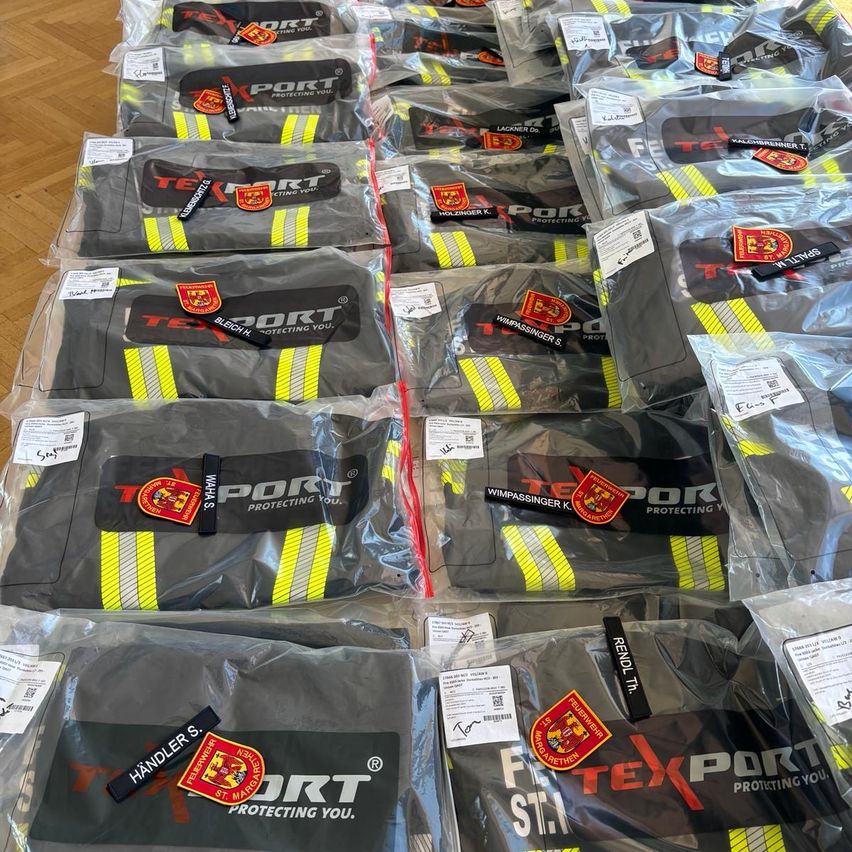 Mehrere Packungen von Schutzausrüstung, wahrscheinlich für Feuerwehrleute, sind ordentlich organisiert und in durchsichtigen Plastik verschlossen. Jede Packung enthält ein Paar Handschuhe mit reflektierenden Streifen und der Markenbezeichnung PORT.
