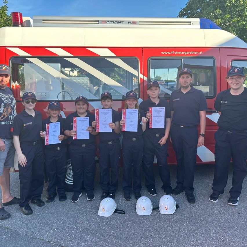 Eine Gruppe von Kindern und Erwachsenen in Feuerwehruniformen posiert mit Zertifikaten vor einem Feuerwehrauto.