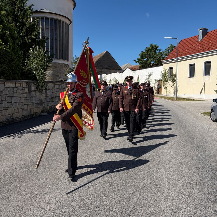 Eine Gruppe von Militärangehörigen mit Flaggen zieht in einer Parade die Straße hinunter. Sie tragen Uniformen und Helme.