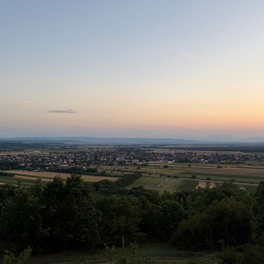 Ein weiter Luftblick auf ein Dorf mit vielen Häusern und Feldern unter einem blauen Himmel mit warmem Sonnenuntergangsglühen.