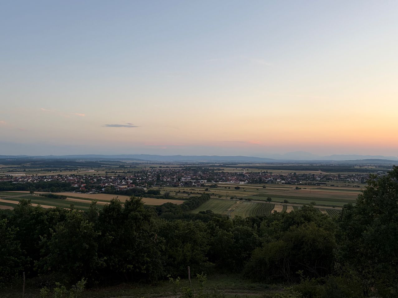 Ein weiter Luftblick auf ein Dorf mit vielen Häusern und Feldern unter einem blauen Himmel mit warmem Sonnenuntergangsglühen.