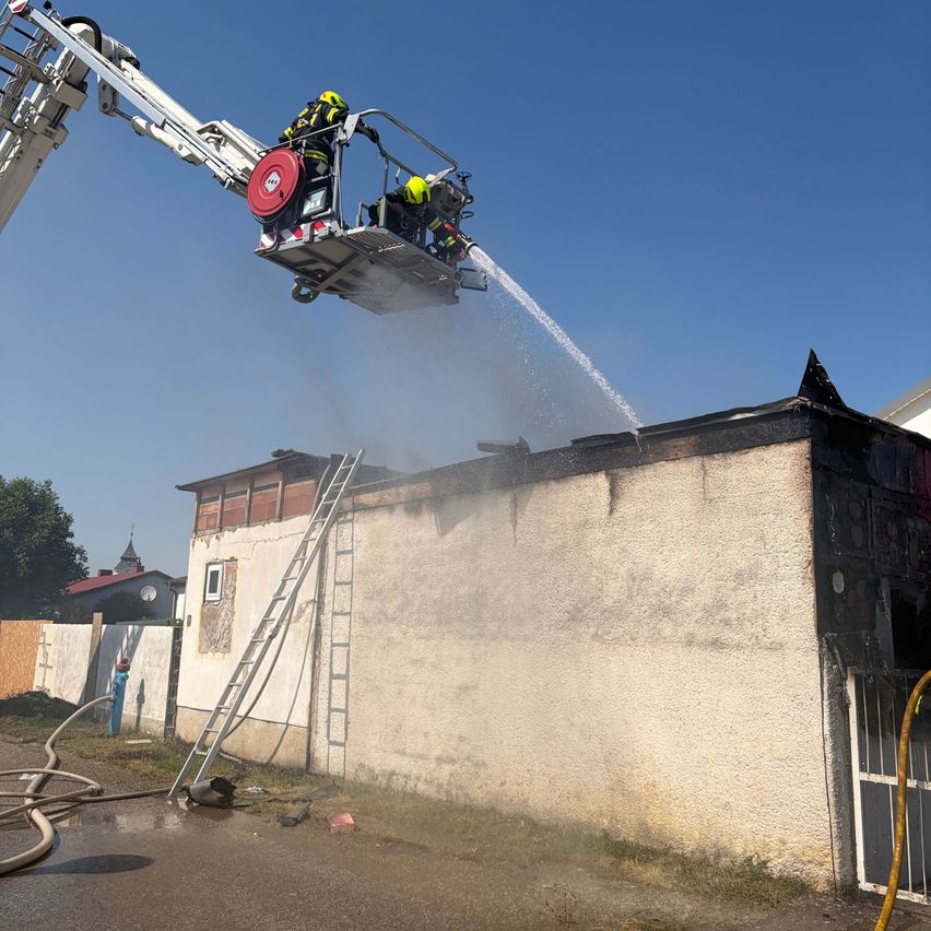 Feuerwehrleute verwenden eine Leiterplattform, um einen Brand auf einem Gebäudedach mit Wasserschläuchen zu löschen.