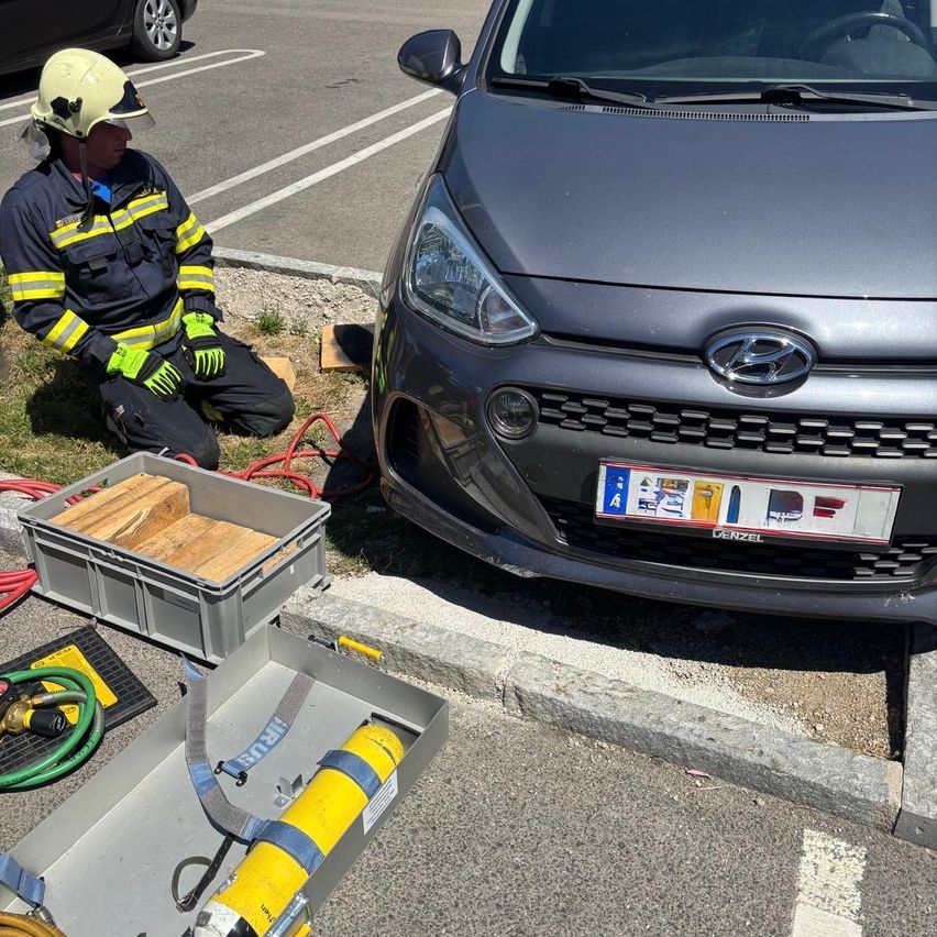 Ein Feuerwehrmann kniet neben einem Hyundai mit einem Kennzeichen und Werkzeug in der Nähe. Ausrüstung und Schläuche sind auf dem Boden ausgelegt.