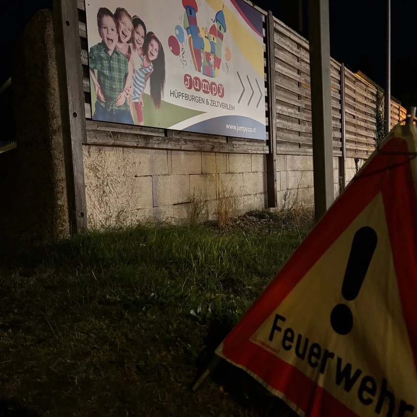 Eine große Werbung für eine Kinderveranstaltung ist an einem Holzzaun angebracht. Die Werbung zeigt eine Gruppe von Kindern, die lächeln, und enthält den Text 'Jump' und 'Hupburgen & Zeltverleih'.