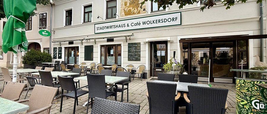 Der Außenbereich eines Restaurants namens Stadtwirtshaus & Cafe Wolkersdorf mit Korbstühlen, Marmorboden und mehreren Tischen.