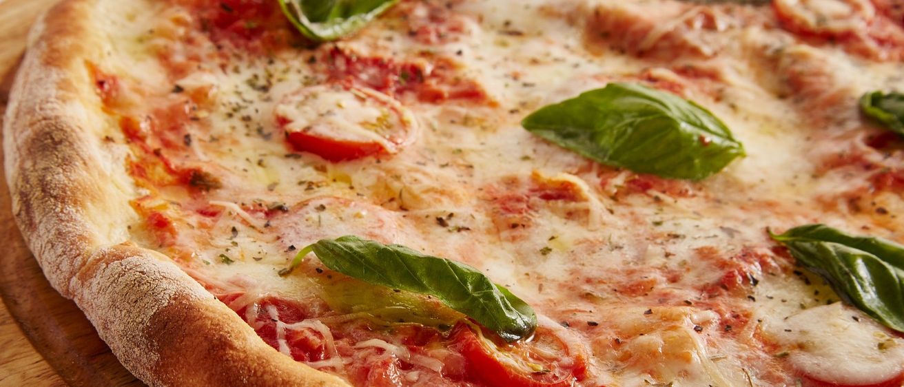 Ein Nahaufnahme einer frisch gebackenen Pizza mit geschmolzenem Käse, Tomatensauce und Basilikumblättern obenauf.