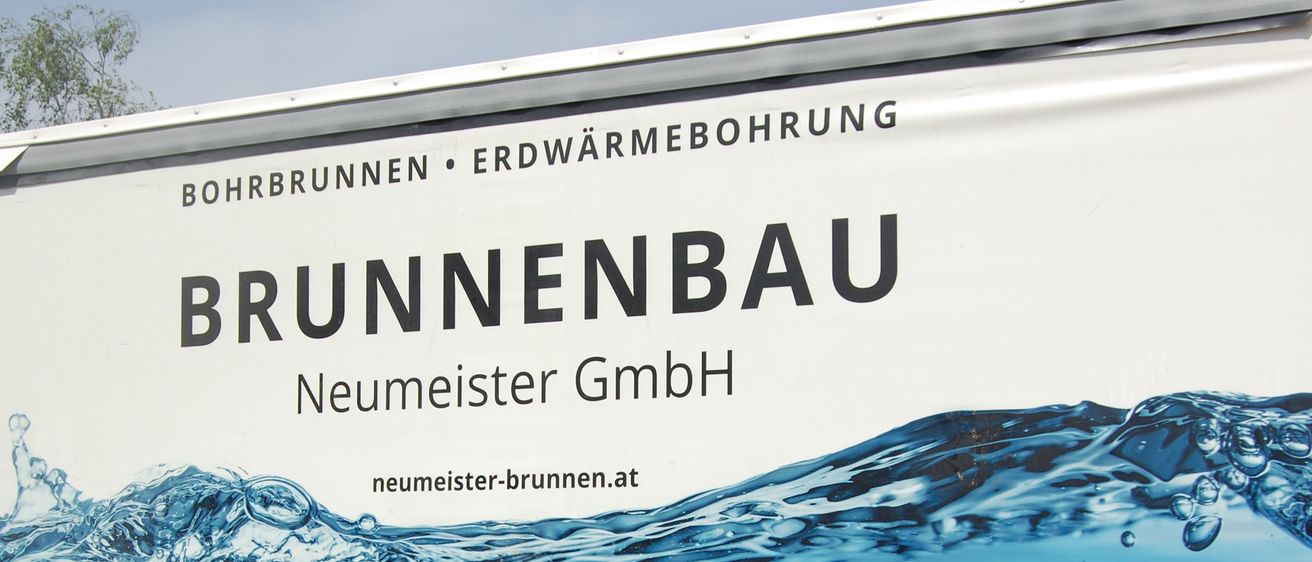 Ein weißer LKW hat den Firmennamen Brunnenbau Neumeister GmbH mit einem blauen Wasserwellen-Design. Er ist in einem Außenbereich geparkt.