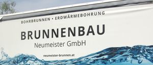 Ein weißer LKW hat den Firmennamen Brunnenbau Neumeister GmbH mit einem blauen Wasserwellen-Design. Er ist in einem Außenbereich geparkt.