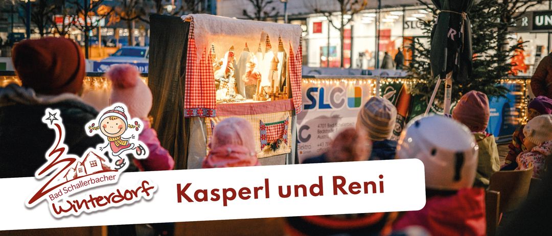 Kinder schauen sich eine Puppenshow an einem Winterabend an. Das Schild sagt 'Kasperl und Reni'. Im Hintergrund sind Bäume und ein Gebäude zu sehen.